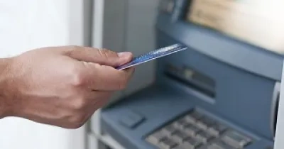 Mano de una persona con una tarjeta bancaria y junto a un cajero automático (Fuente: Servimedia)