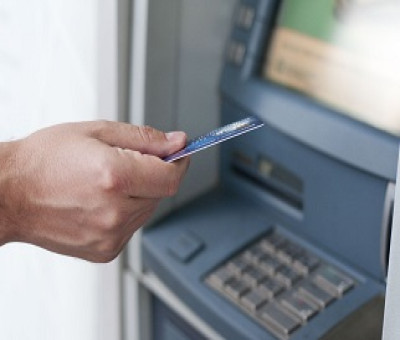 Mano de una persona con una tarjeta bancaria y junto a un cajero automático (Fuente: Servimedia)