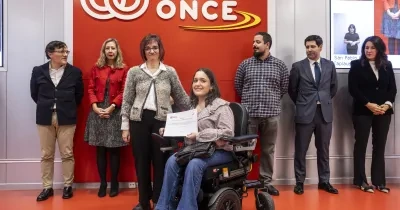 una alumna en silla de ruedas con un certificado en la mano, detras ptras personas con el logo de fundación once