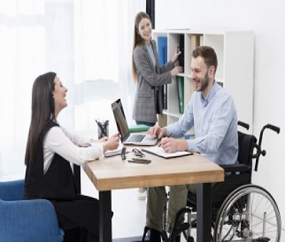 Una persona con discapacidad y en silla de ruedas, trabajando con dos de sus compañeras en la oficina (Fuente: Servimedia)