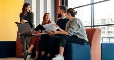 4 personas jóvenes dialogando en un sofa con un ordenador delante