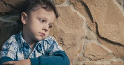 Un niño sentado apoyado en un muro