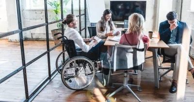 Cuatro personas trabajando en una oficina, manteniendo una reunión. Una de ellas va en silla de ruedas, ejemplarizando la inclusión laboral