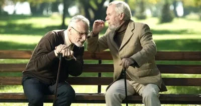Dos hombres mayores sentados en un parque, acercándose el uno al otro para oirse al hablar