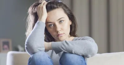 Una mujer sentada en el sofá de rodillas tocándose el pelo