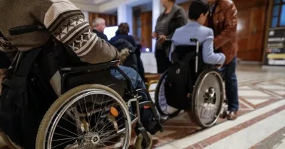 Dos personas con silla de ruedas caminando por u palacio muy regio en el que les reciben ciertas personas