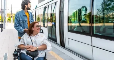 Un hombre sin discapacidad junto a una mujer en silla de ruedas esperando en el andén al tren