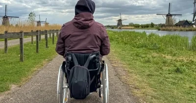 Persona en silla de ruedas de espaldas mientras camina al frente por un sendero