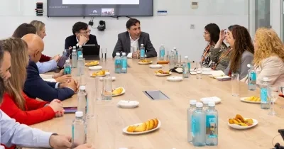 Varios representantes sentados en una mesa hablando, se observan papeles, botellas de agua y comida en el centro de la mesa
