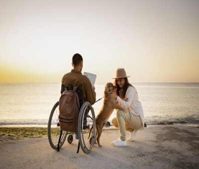 Una persona en silla de ruedas disfrutando de su tiempo de ocio turístico frente al mar, junto a su pareja y su perro (Fuente: Servimedia)