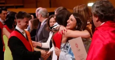 Una foto de dos alumnos recibiendo el título de los profesores de la universidad y dándose un abrazo