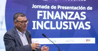 Alt text:  Persona interviniendo desde un atril durante la jornada de presentación de “Finanzas Inclusivas”. La imagen muestra a la persona junto a dos micrófonos mientras realiza una exposición ante el público. Al fondo aparece una gran pantalla azul con el texto “Jornada de Presentación de Finanzas Inclusivas” y los logotipos de las entidades organizadoras. El acto forma parte de la presentación de la renovación del recurso formativo impulsado por Fundación ONCE para promover la educación financiera inclu