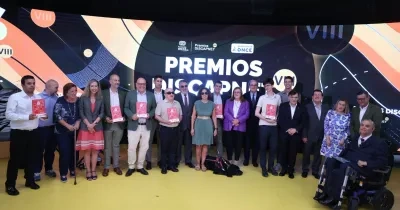 Foto de grupo de las personas premiadas, representantes institucionales y asistentes durante la VIII edición de los Premios Discapnet de Fundación ONCE. Los participantes posan sobre un escenario frente a una gran pantalla con el texto “Premios Discapnet VIII” y los logotipos de Fundación ONCE y Grupo Social ONCE. Varias personas sostienen los galardones, mientras que en la primera fila también aparecen una persona usuaria de silla de ruedas eléctrica y un perro guía tumbado en el suelo