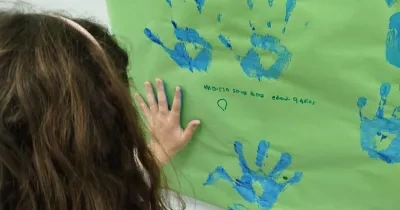 nila con manos llenas de pintura dejando su huella en un papel en la pared