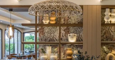 el hotel ILUNION Caleta Park por dentro, donde se puede ver unas mesas de restaurante al fondo y al frente una lámpara grande con una estantería decorada rústicamente con jarrones y tinajas