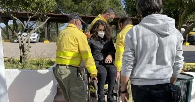 Tres técnicos de emergencias levantando a pulso a una usuaria en silla de ruedas, haciendo un ejemplo práctico con un supervisor que explica