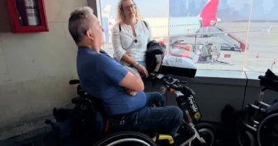 Persona con silla de ruedas esperando a embarcar en un avión, que puede verse al fondo por una cristalera