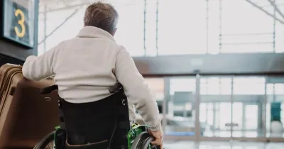 Un hombre con silla de ruedas, al que se ve de espaldas, movíendose por el aeropuerto con su maleta