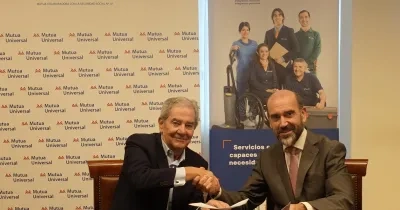Dos representantes de Mutua Universal y Grupo SIFU estrechan la mano durante la firma de un acuerdo de colaboración. Ambos están sentados frente a una mesa con documentación, junto a paneles corporativos de las dos entidades relacionados con la integración laboral y la inclusión de personas con discapacidad.