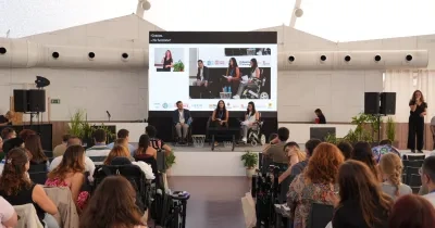 Participantes asisten a una mesa redonda del II Congreso Estatal de Juventud con Discapacidad en Valladolid. En el escenario, tres ponentes intervienen en un debate sobre los 20 años de la Convención de la ONU sobre los Derechos de las Personas con Discapacidad, mientras una intérprete de lengua de signos presta apoyo comunicativo. Al fondo, una gran pantalla reproduce la sesión y, entre el público, se observan asistentes con y sin discapacidad siguiendo la jornada.