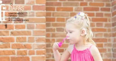 niña con un audífono debido a su discapacidad auditiva soplando un utensilio para hacer burbujas de jabón. También sale el logo de FIAPAS arriba a la izquierda