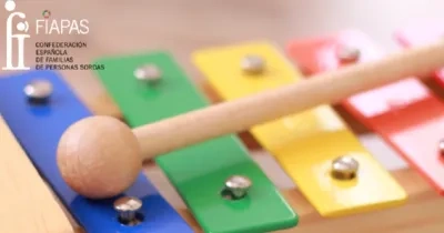 Xilófono de colores con mazo de madera, acompañado del logo de FIAPAS (Confederación Española de Familias de Personas Sordas).