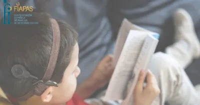 niño con discapacidad auditiva leyendo un libro en un sofça, arriba a la izquierda sale el logo de FIAPAS
