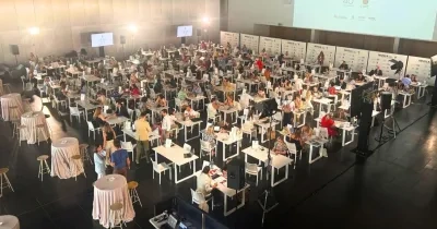 Salón de juntas con varias mesas y muchos ponentes y oyentes