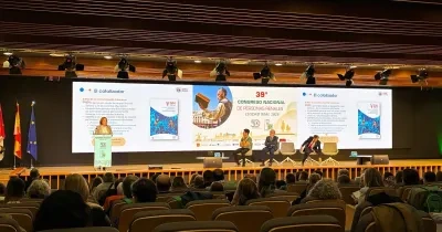 Vista general de un auditorio durante una ponencia del 39º Congreso Nacional de Personas Renales, celebrado en Ciudad Real en 2026. En el escenario, una persona interviene desde un atril mientras varias personas permanecen sentadas en una mesa redonda. Al fondo, una gran pantalla proyecta una presentación sobre el espacio GN Conecta y el papel de “El catalizador”. El público ocupa gran parte de las butacas del auditorio, orientadas hacia el escenario iluminado. A la izquierda se observan las banderas de Esp