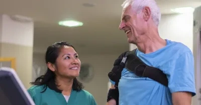 Un señor mayor siendo tratado por una mujer rehabilitadora