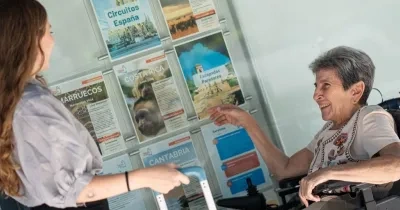 Una dependienta de la agencia de viajes enseñando folletos a una señora en silla de ruedas