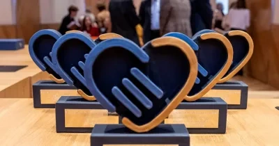 Los 5 premios que se entregarán en la gala delante y, al fondo, personas organizadoras