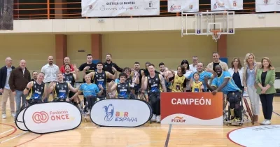 Equipo y cuerpo técnico del CD Ilunion posan en una pista cubierta de baloncesto tras proclamarse campeones de la Supercopa de España de baloncesto en silla de ruedas. En el centro de la imagen, varios jugadores en silla de ruedas sostienen un trofeo y realizan un gesto con cuatro dedos levantados. En la parte frontal aparecen paneles con los logotipos de Fundación ONCE, BSR España y un cartel con la palabra “CAMPEÓN”. Al fondo se observan canastas y pancartas institucionales de Castilla-La Mancha y BSR Esp