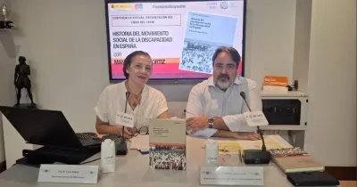 Mesa de presentación de una publicación del CERMI sobre la historia del movimiento social de la discapacidad en España. Dos personas participan en una conferencia junto a ejemplares del libro, micrófonos y material de trabajo. Al fondo, una pantalla muestra la portada de la obra y el título de la presentación virtual.