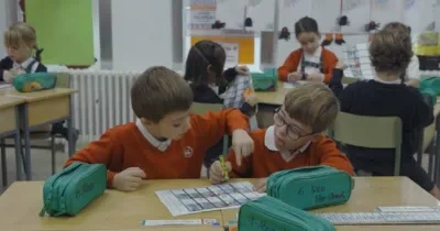 camapaña de plena inclusión, imagen de dos niños en la escuela jugando en un escritorio con un papel y pinturas