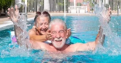 Dos personas disfrutando de una piscina mientras una tapa los oídos a otra (Fuente: Oticon)