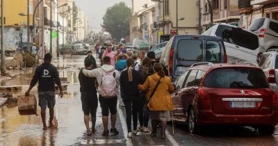 una familia caminando por valencia observando coches apilados, charcos y resto de la catástrofe