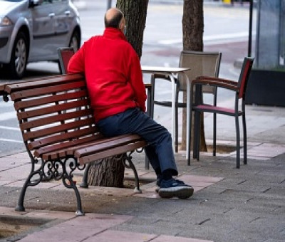 Una persona mayor sola, sentada en un banco de la calle