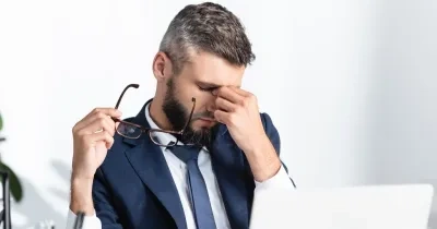 hombre llevándose la mano a la cara delante del ordenador, simulando un estrés laboral