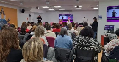 Encuentro entre la Fundación Cermi Mujeres y los Cermis Autonómicos en una sede donde están muchas personas sentadas y al fondo 3 mujeres de pie con una pantalla digital