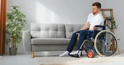 hombre con movilidad reducida en silla de ruedas intenta colocarse para pasar de la silla de ruedas al sofá de forma autónoma