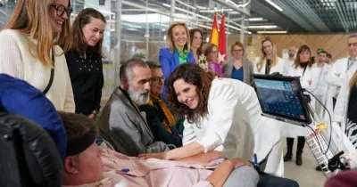 La presidenta de la Comunidad de Madrid, Isabel Díaz Ayuso, visitando el Hospital Enfermera Isabel Zendal y saludando a un paciente con ELA que es residente del centro. A su lado hay varias familias y médicos visualizando la visita oficial