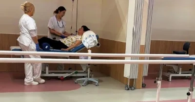En un box de un hospital, una doctora y una enfermera hablan con una paciente encamada