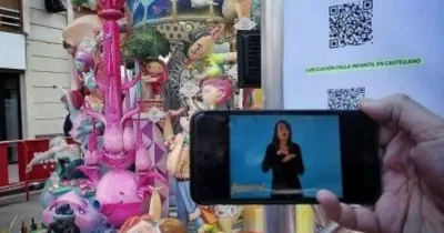 una falla de fondo mientras se está apuntando con un movil al código QR y está describiendo en la pantalla una mujer la falla valenciana