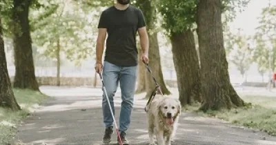 Una persona ciega camina por un parque con su perro guía (Fuente: Servimedia)