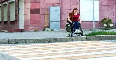 Una chica joven en silla de ruedas dispuesta a pasar por un paso de peatones, pero no puede debido al bordillo que impide seguir su camino