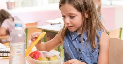 niña mirando un táper con comida saludable (fruta) en la escuela