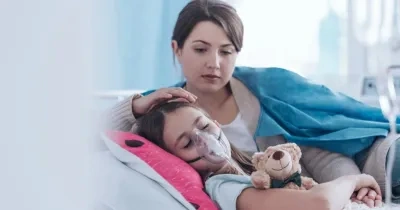 Madre cuidando a su hija con fibrosis quística que está en la cama usando un tratamiento respiratorio