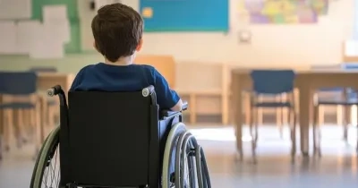Un niño, de espaldas, sentado en una silla de ruedas, dentro de un aula escolar