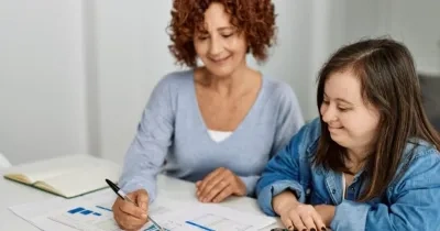 persona con síndrome de down siendo atendida por una profesora que la está enseñando cosas en un libro